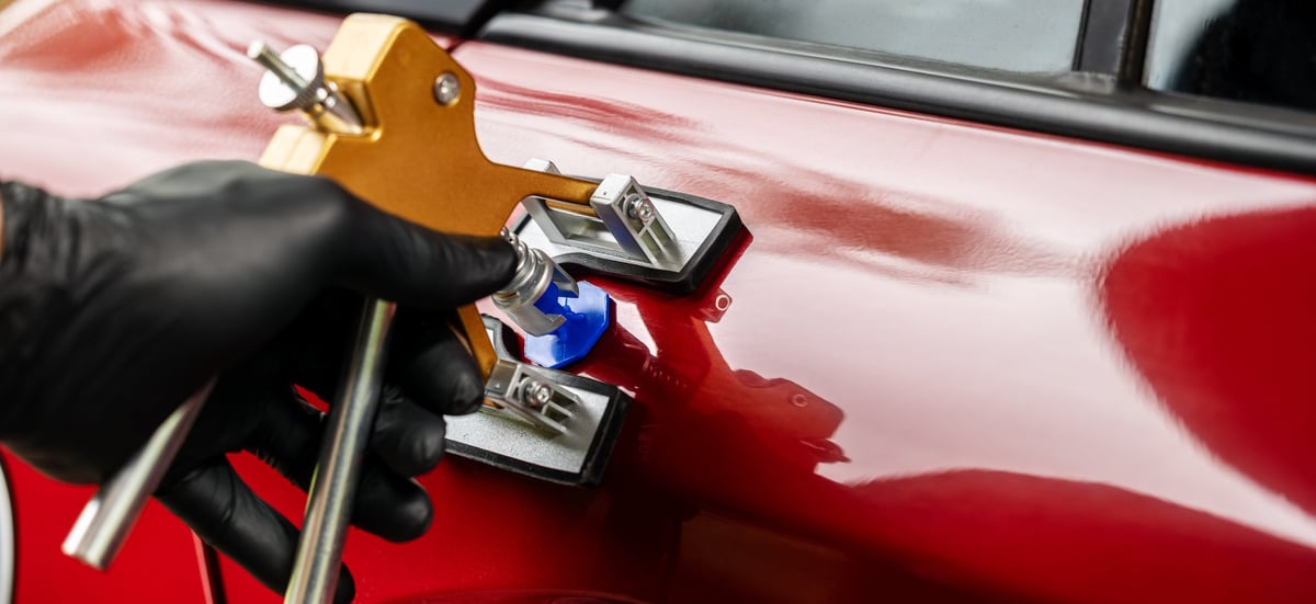 Technician performing paintless dent repair on vehicle in a clean auto body shop